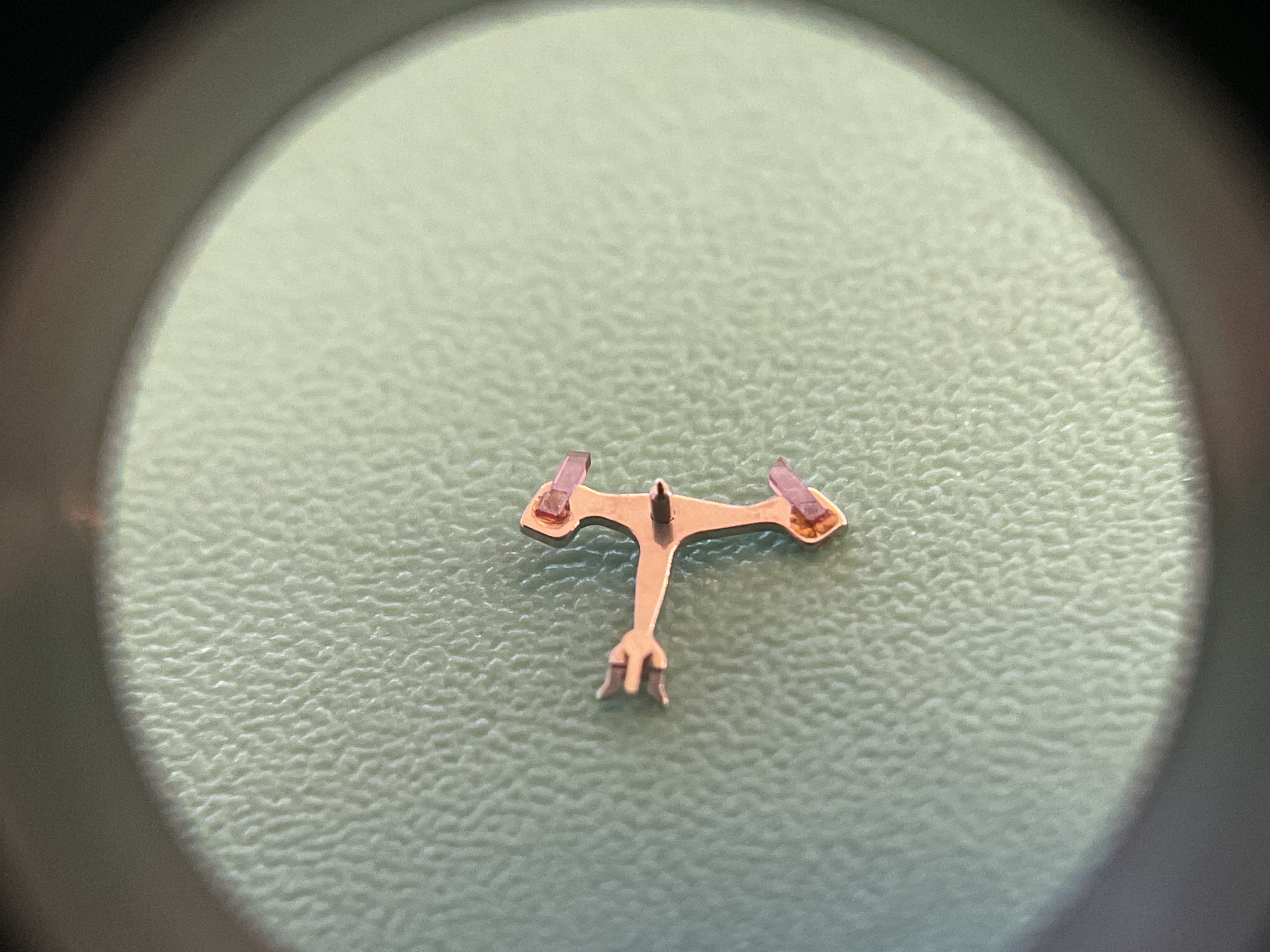 The pallet fork under magnification, its ruby stones reset in fresh shellac.