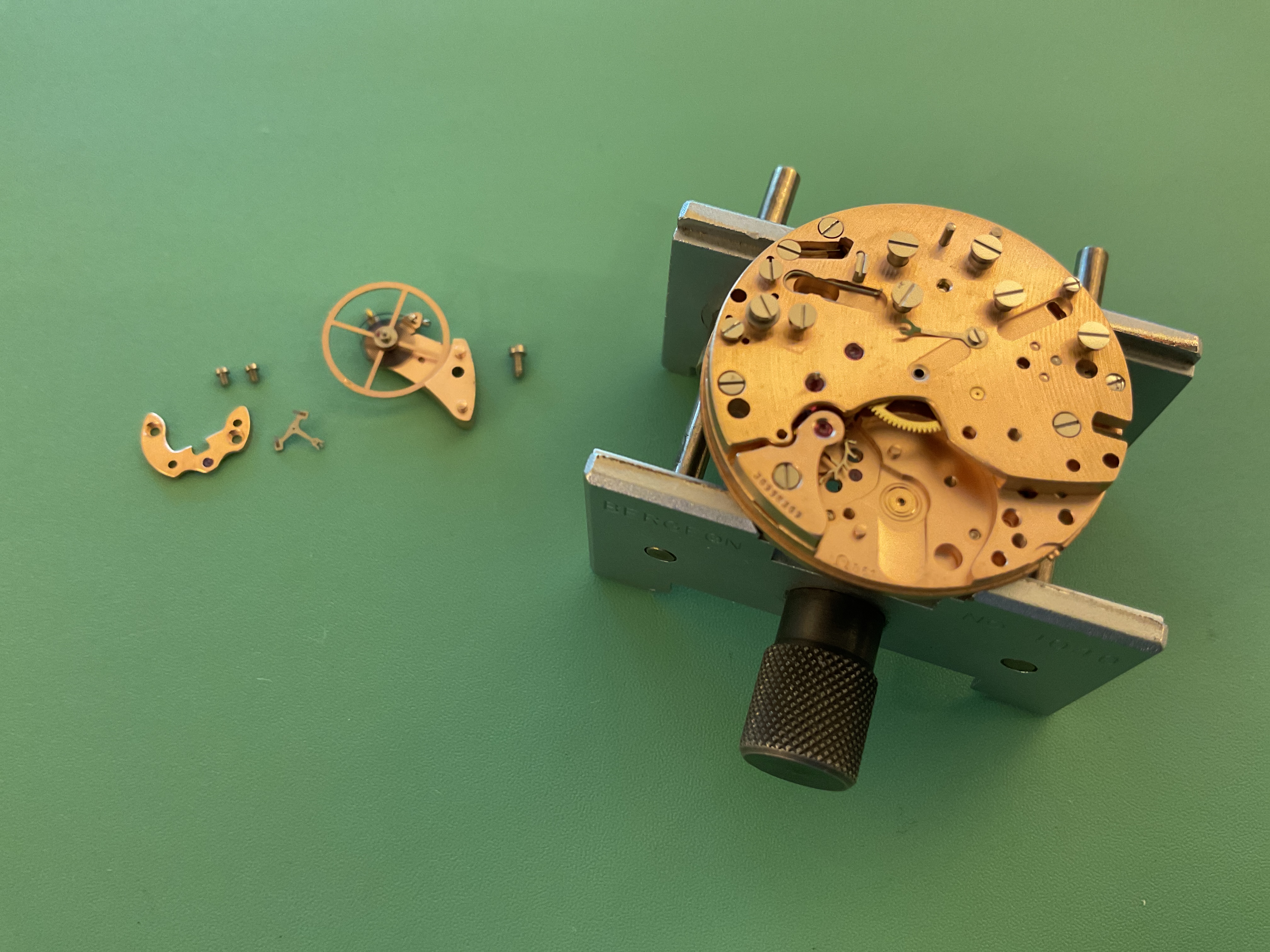 The cleaned movement in a holder, with the balance and bridges set aside for reassembly.