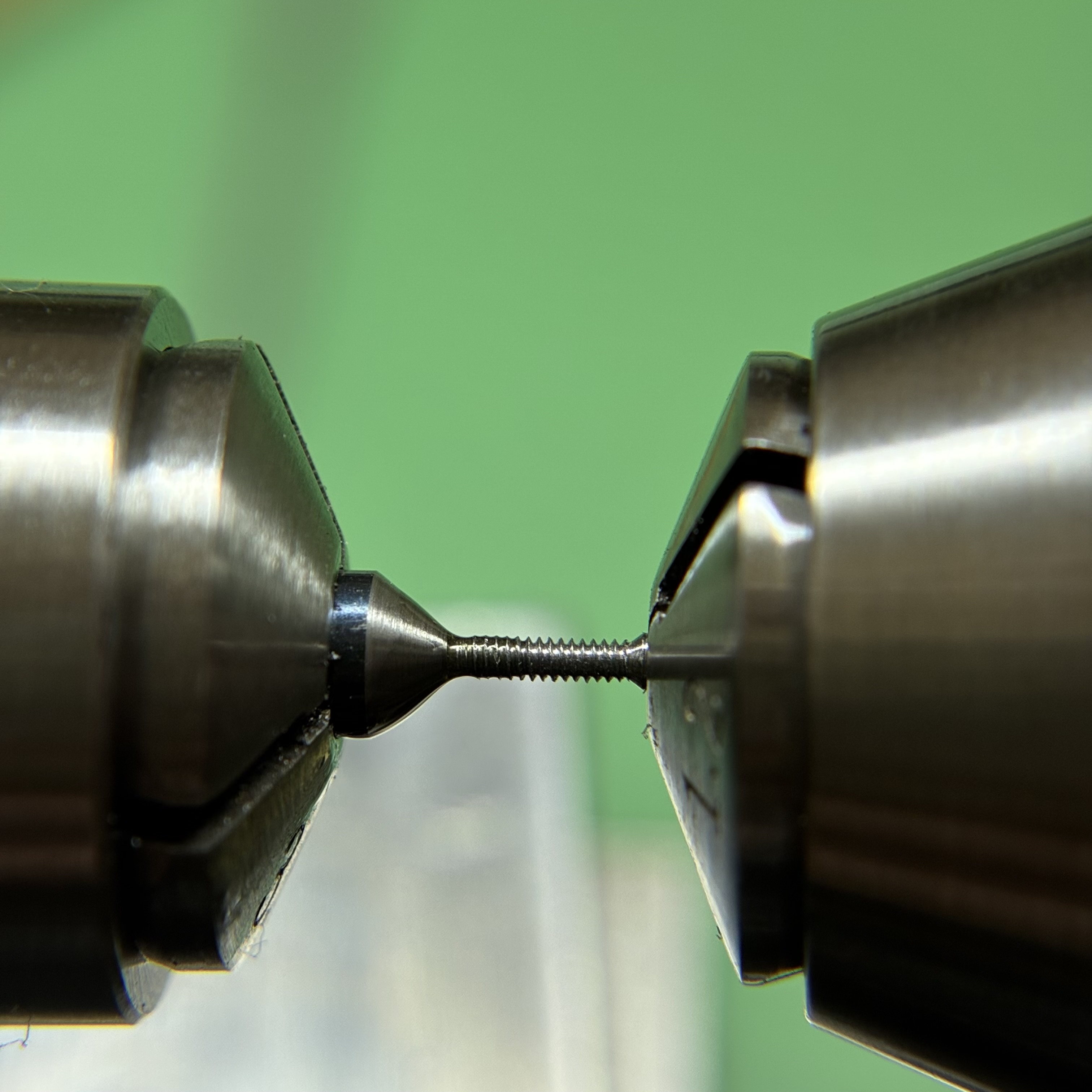 A steel screw blank between lathe collets, freshly threaded.